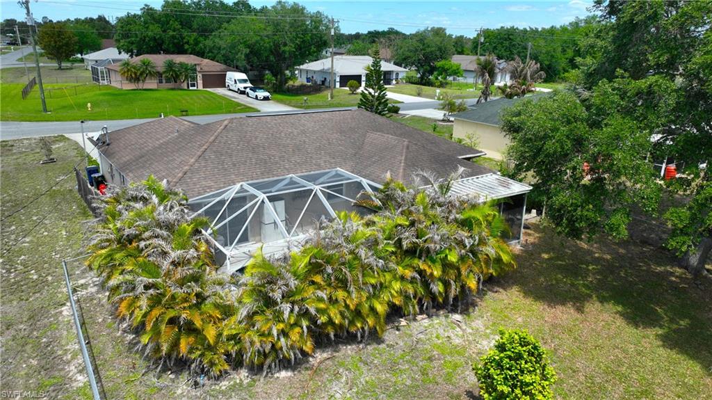The property features a screened-in pool enclosure, a shingled roof, and an expansive yard with mature trees