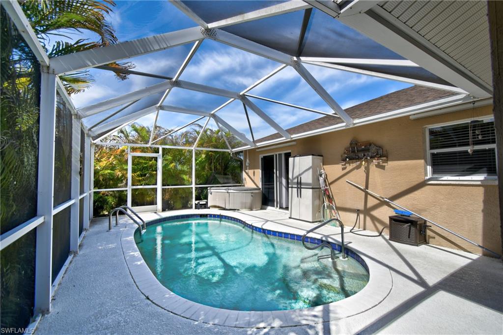 This property features a screened-in pool area with a curvilinear pool, a hot tub, and a surrounding paved deck
