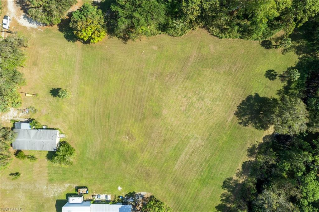 Expansive green space featuring large cleared areas, mature trees bordering the property, and two structures visible on the perimeter
