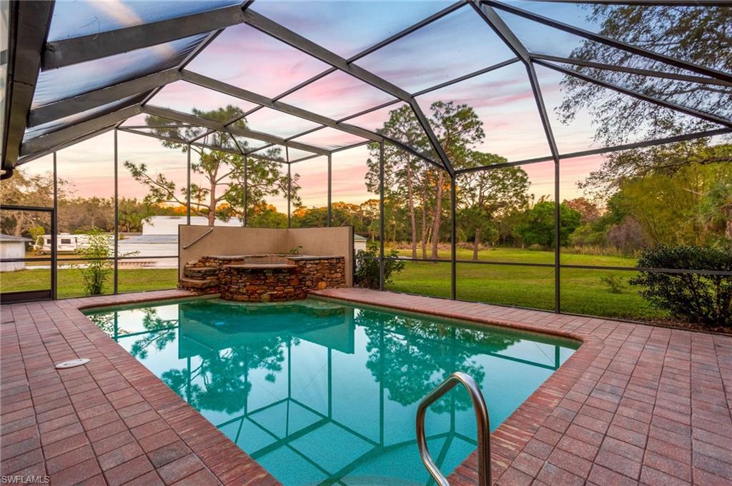 Screened enclosure featuring a rectangular pool with integrated spa and stone surround