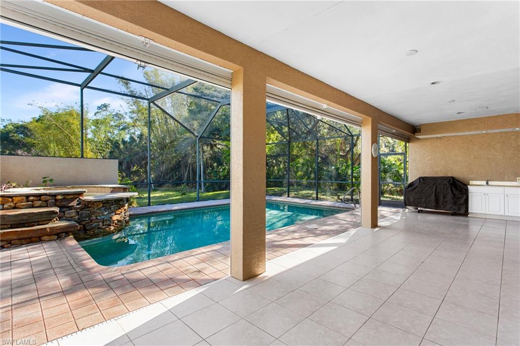 Screened lanai featuring a swimming pool, stone water feature, outdoor counter space with white cabinetry, and a spacious tiled patio