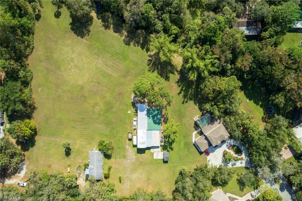 Expansive property featuring a large, cleared grassy area, mature perimeter trees, and multiple structures