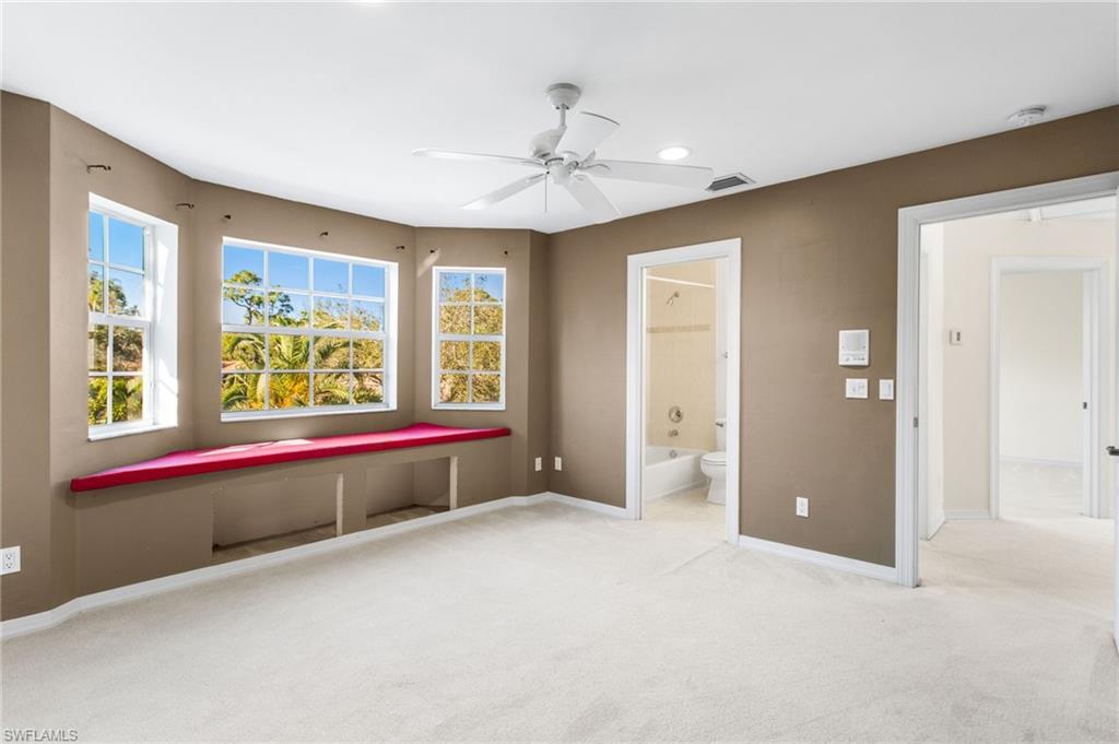 Spacious room featuring a bay window with an integrated window seat, carpeted flooring, a ceiling fan, and painted walls