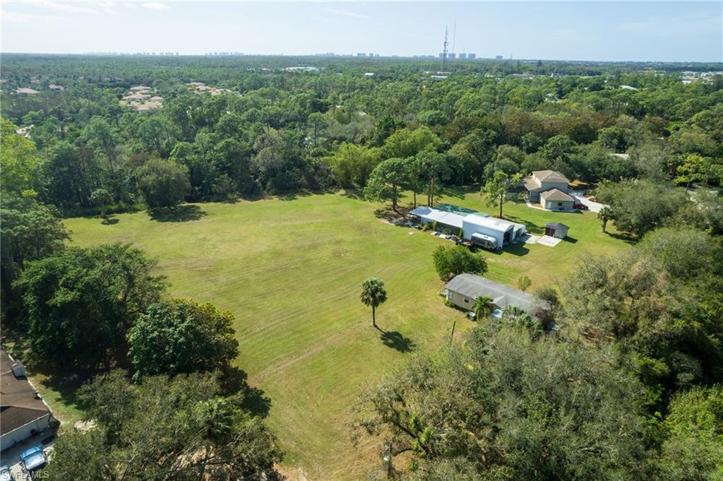 Expansive grassy field surrounded by mature trees, featuring two residential structures and an additional outbuilding
