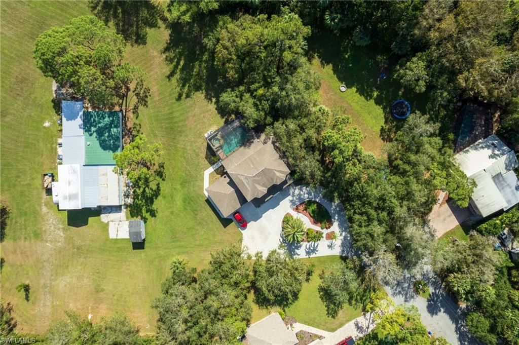 Aerial perspective showcasing a property featuring a brown shingle roof, a paved driveway, a manicured front lawn with mature landscaping, and an enclosed pool area