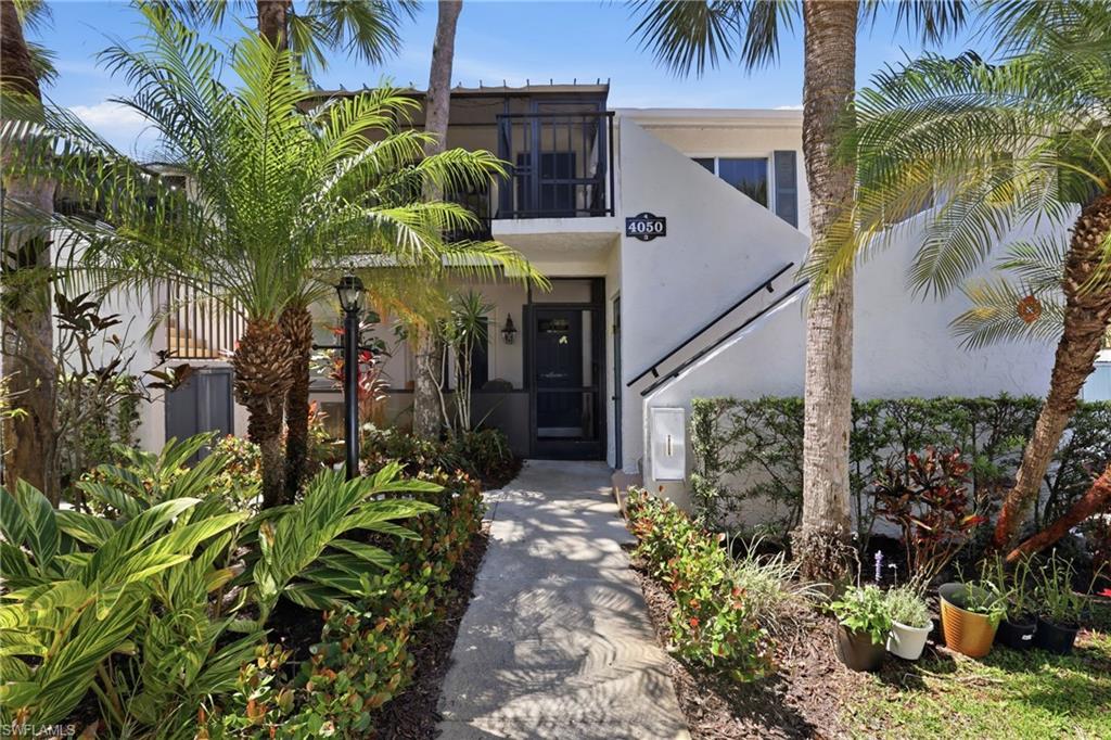 White stucco exterior featuring a private entrance, exterior staircase with dark handrail, and a second-story balcony with dark railings