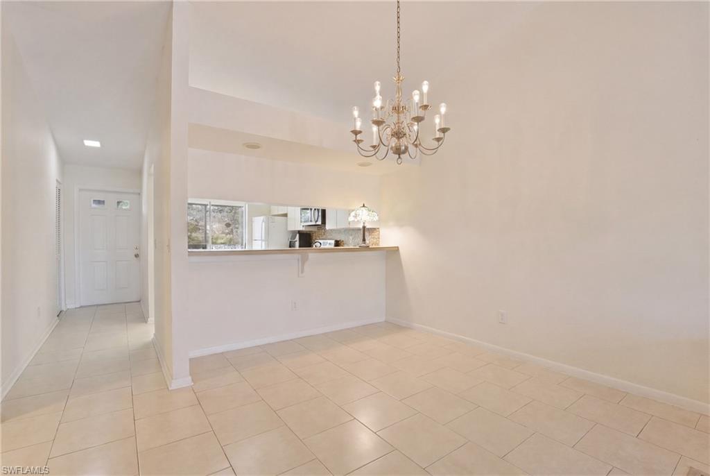 Open-concept dining area featuring a multi-bulb chandelier, tile flooring, and a pass-through counter to the kitchen