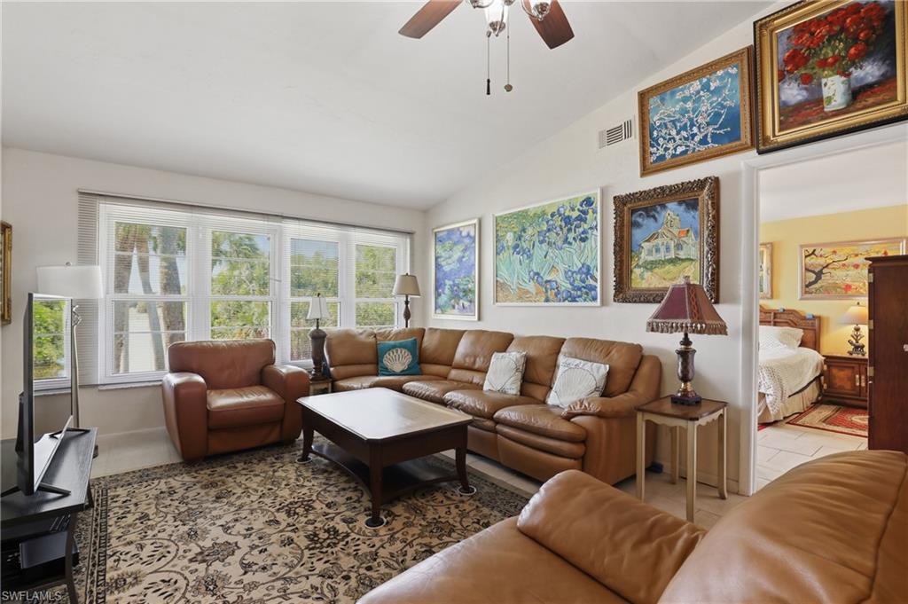 Vaulted ceiling living area featuring multiple windows, a ceiling fan, and a neutral color palette