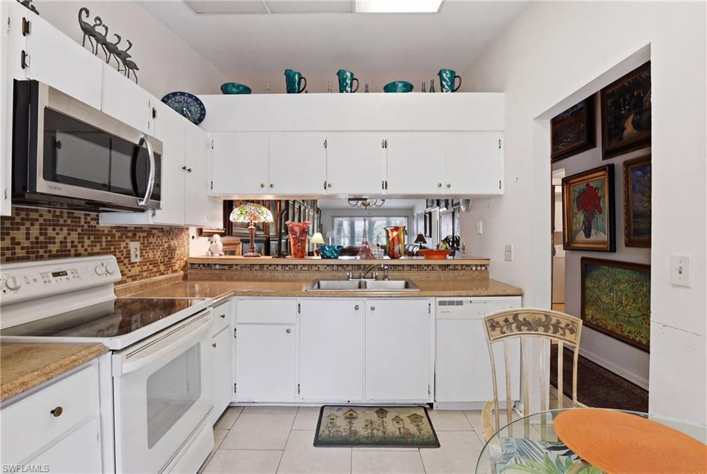 Kitchen featuring white cabinetry, a stainless steel microwave, a glass cooktop range, a tile backsplash, and light-toned countertops
