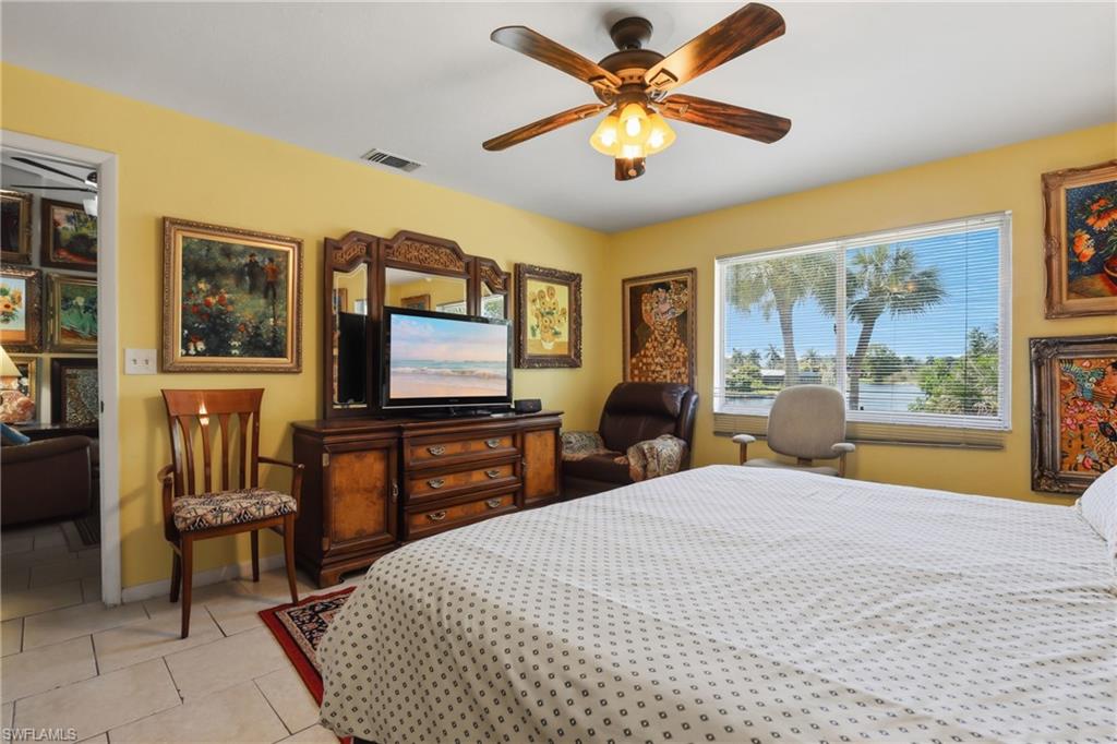 Room featuring tiled flooring, a ceiling fan with light fixture, and a window offering water views with tropical foliage