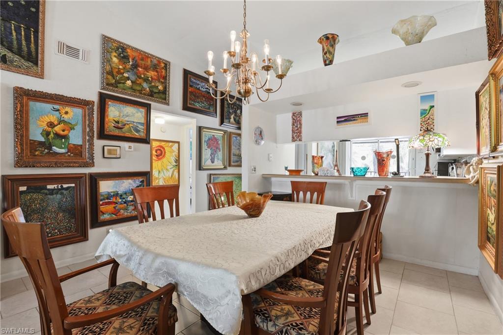 Dining area featuring a brass chandelier, tile flooring, and a pass-through counter opening