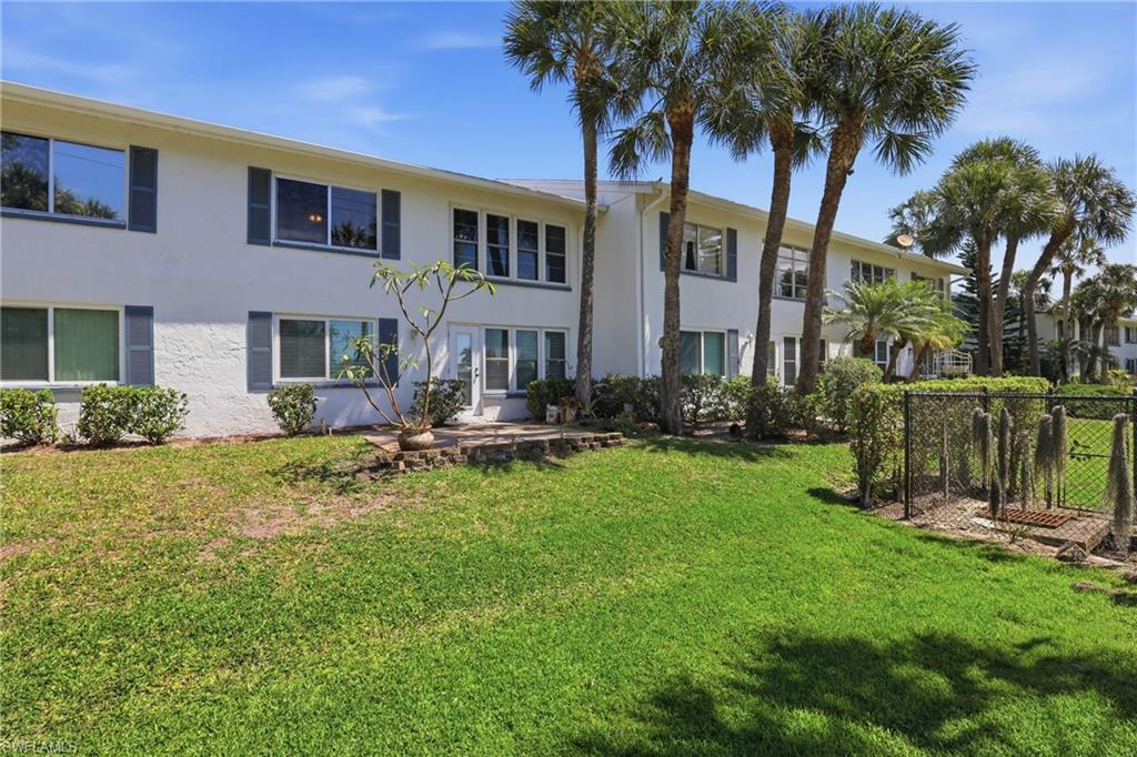 Two-story stucco building with multiple windows, framed by mature palm trees and lush green lawn