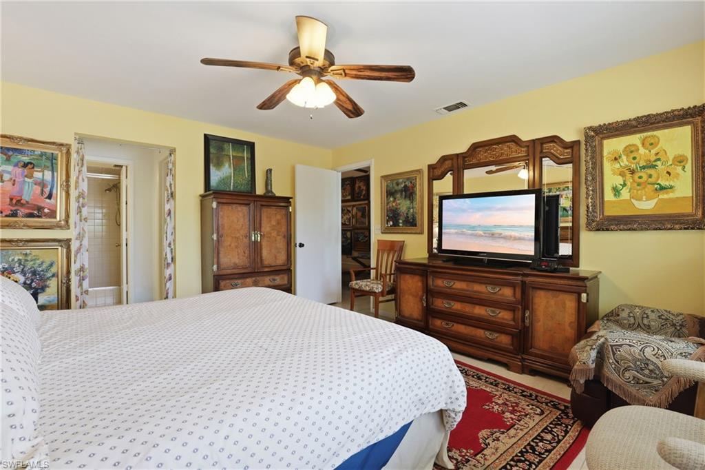 Spacious room featuring a ceiling fan with light fixture, light yellow wall color, and a partial view of a bathroom with a tiled shower
