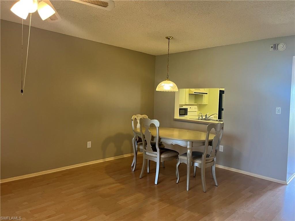 Dining area featuring wood-finish flooring, a ceiling fan with integrated lighting, and a pendant light fixture