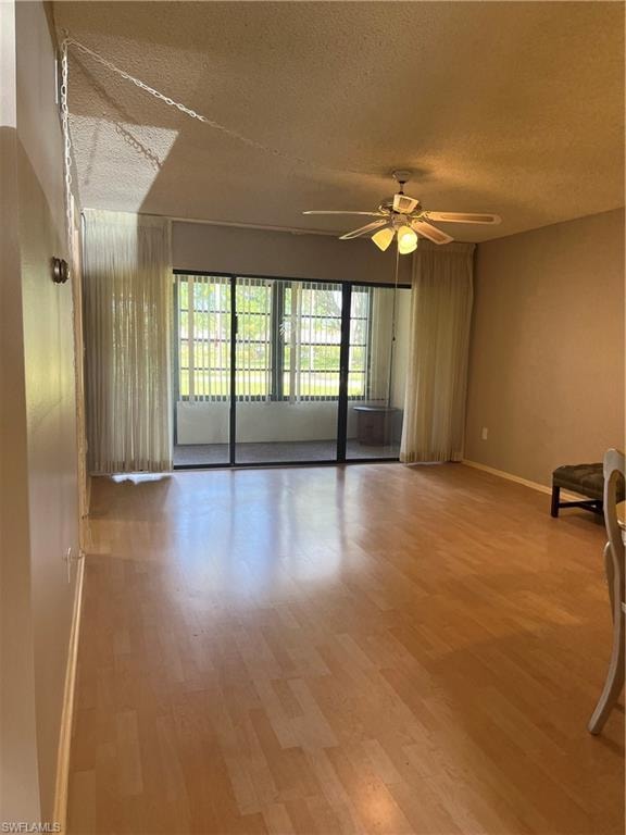 Bright interior space featuring wood-finish flooring, a ceiling fan with integrated lighting, and sliding glass doors opening to an enclosed patio