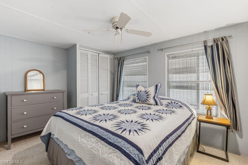 Bedroom featuring light blue paneling, two windows with blinds, a ceiling fan, and louvered bifold closet doors.