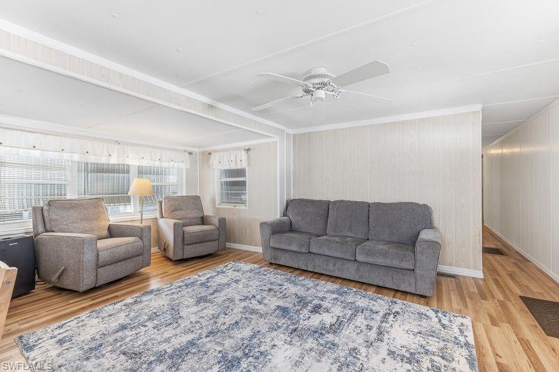 Living area featuring wood-finish laminate flooring, white paneled walls, and a ceiling fan.
