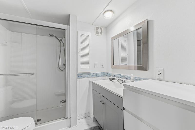 Bathroom featuring a glass-enclosed shower, vanity with a white countertop, under-sink storage, a framed mirror, and a decorative tile backsplash, and tiled floors.