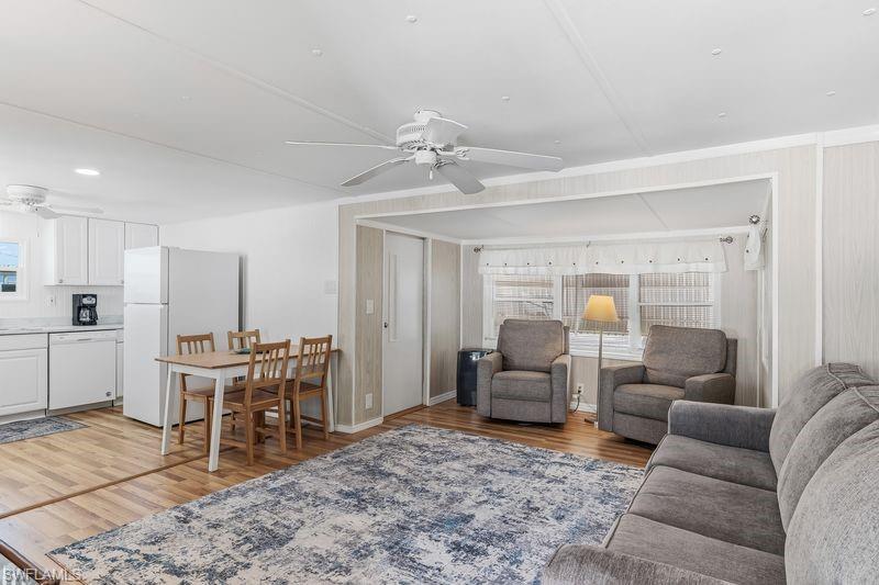 Open-concept living area featuring wood-finish laminate flooring, a ceiling fan, and white cabinetry in the kitchen space.