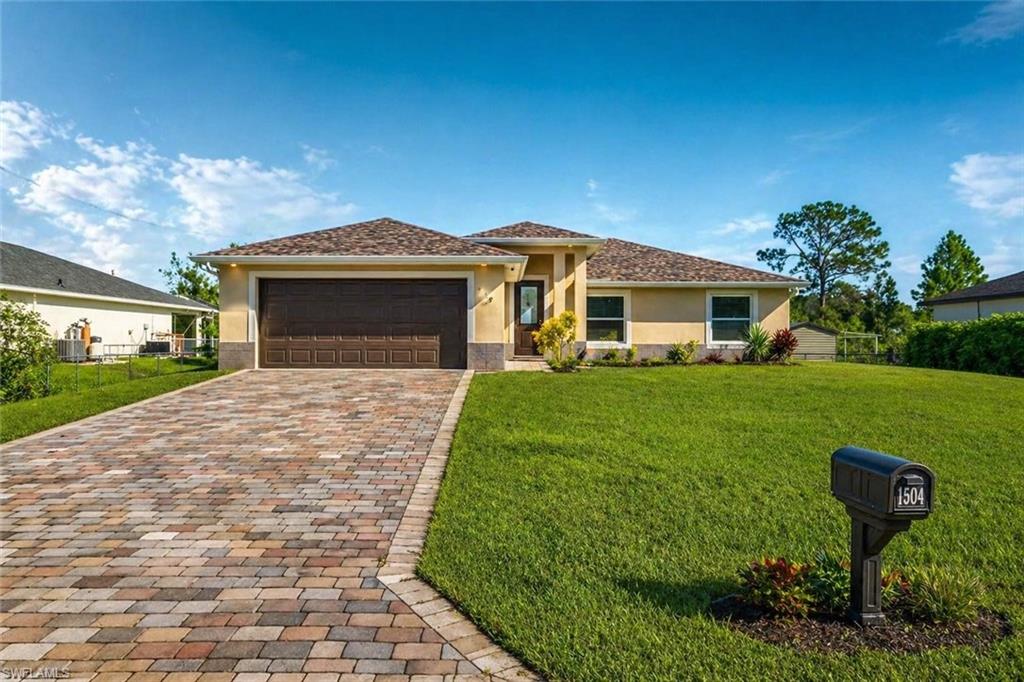 Single-story residence featuring a paver driveway, an attached garage with a dark wood-finish door, and a light-colored stucco exterior with stone accents