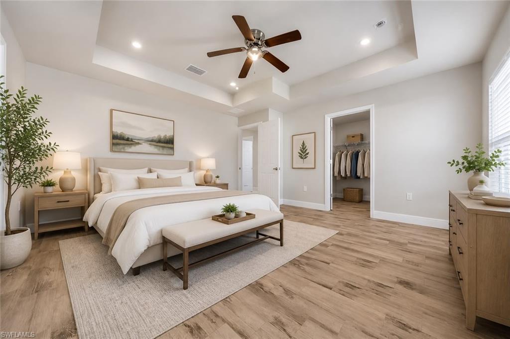 Spacious bedroom featuring a tray ceiling with recessed lighting and a ceiling fan, wood-finish flooring, and light-filtering window blinds