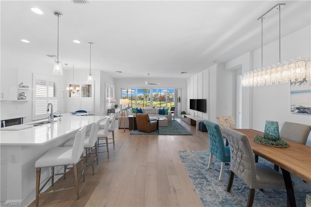 Open-concept living area featuring light wood-finish flooring, recessed lighting, and a white kitchen island with pendant lighting