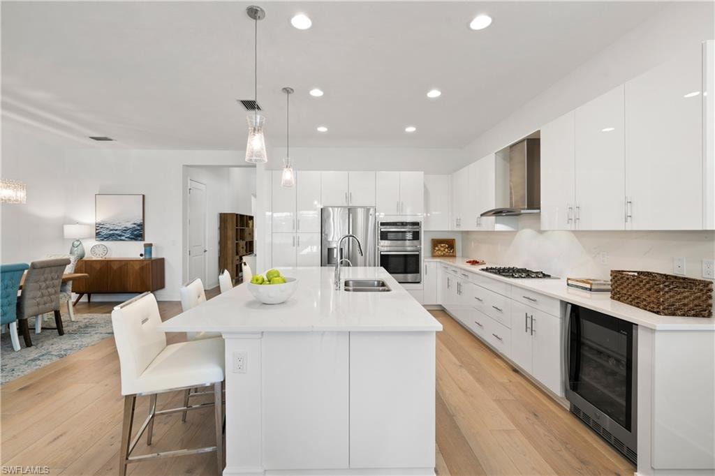 Open-concept kitchen featuring white cabinetry, a central island with bar seating, stainless steel appliances, and wide wood flooring