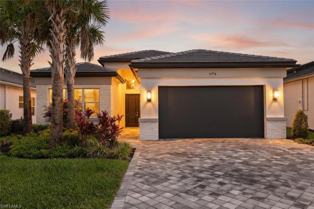 Contemporary stucco exterior with tile roof, paver driveway, and accent stone veneer