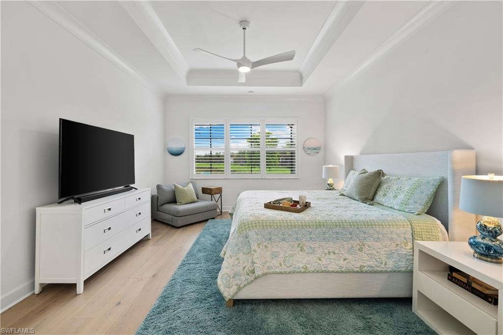 Spacious room featuring wood flooring, a tray ceiling with a modern ceiling fan, and white window shutters