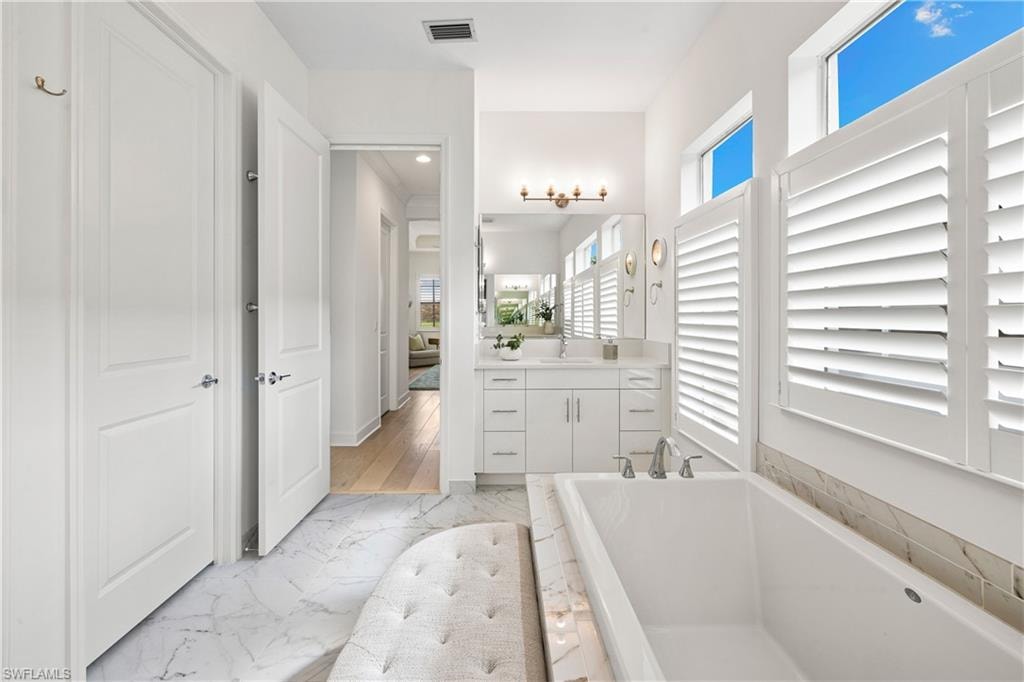 White soaking tub, second sink area, tile flooring, and white plantation shutters