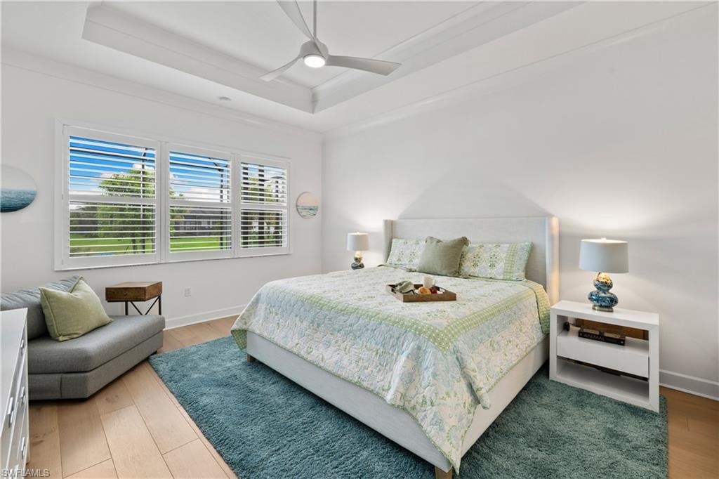 Spacious room featuring wood flooring, a tray ceiling with a ceiling fan, and large windows with plantation shutters