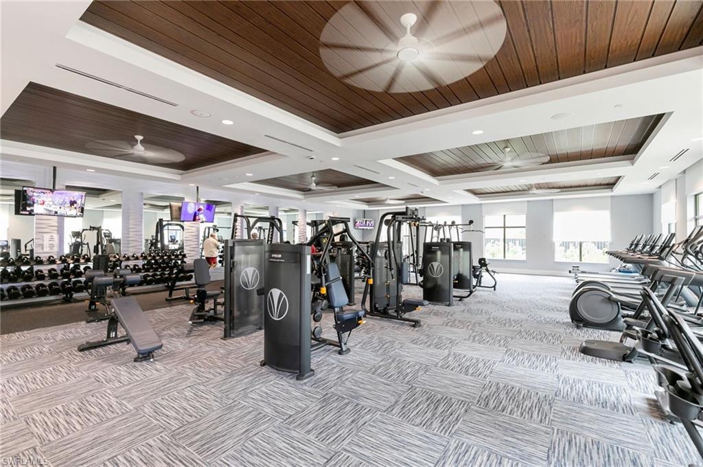 Spacious fitness center featuring a patterned carpet, recessed lighting, and a tray ceiling with wood-finish panels