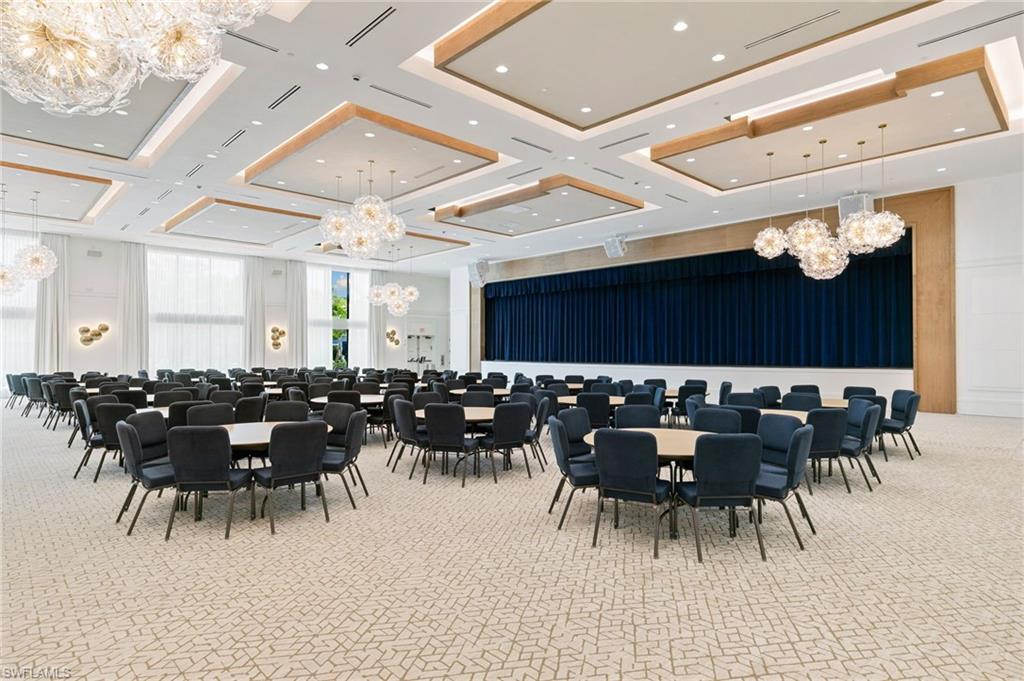 Spacious event hall featuring a stage with dark blue curtains, recessed lighting, decorative ceiling panels, and multiple ornate chandeliers