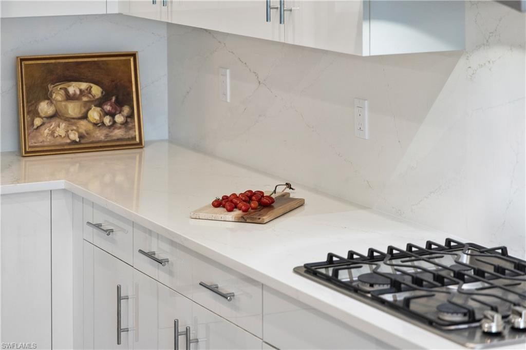 White engineered stone countertops with a complementary white backsplash, sleek flat-panel cabinetry, brushed nickel hardware, and an integrated gas cooktop