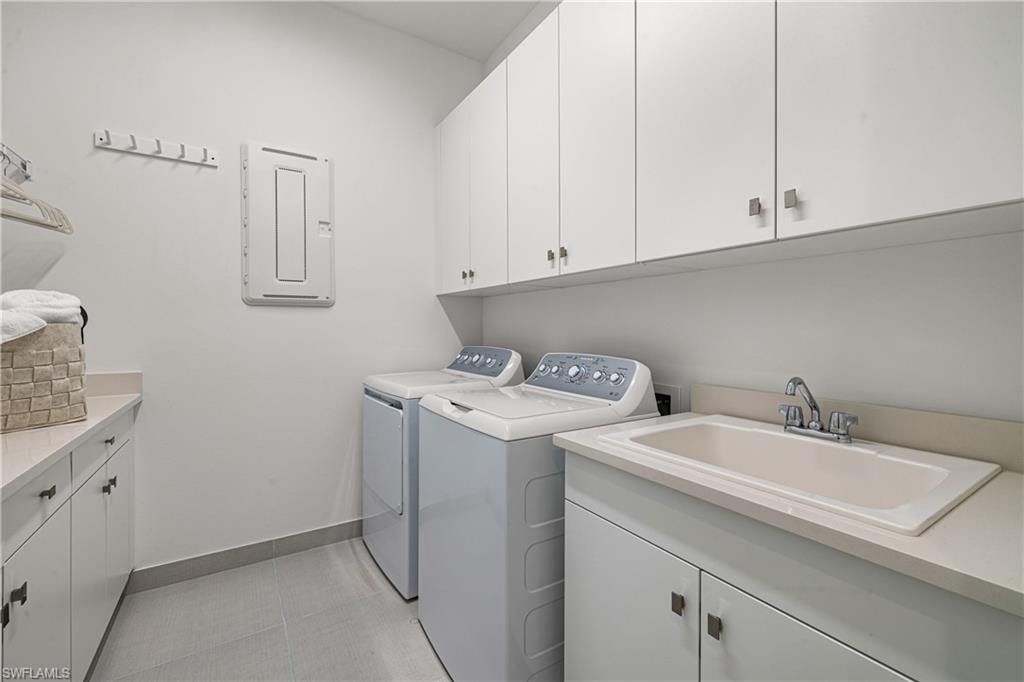 Dedicated utility space featuring a built-in sink, ample white cabinetry for storage, light-toned countertops, and neutral floor tiling