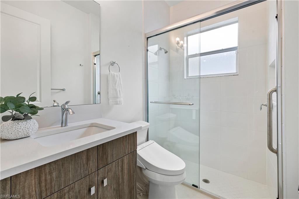 Bathroom featuring a vanity with a quartz countertop and integrated sink, chrome faucet, wall-mounted mirror, and a glass-enclosed shower with white tiled walls and a window