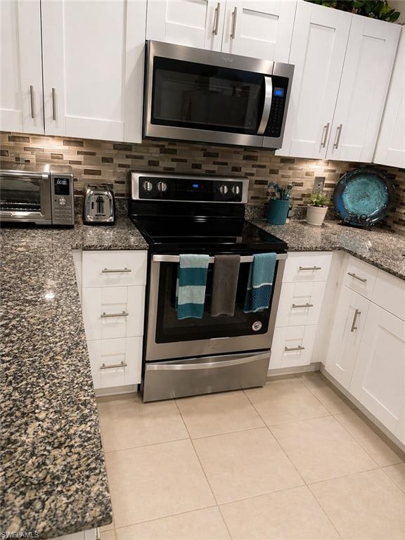 Modern kitchen featuring stainless steel appliances, white cabinetry, speckled countertops, and a tiled backsplash