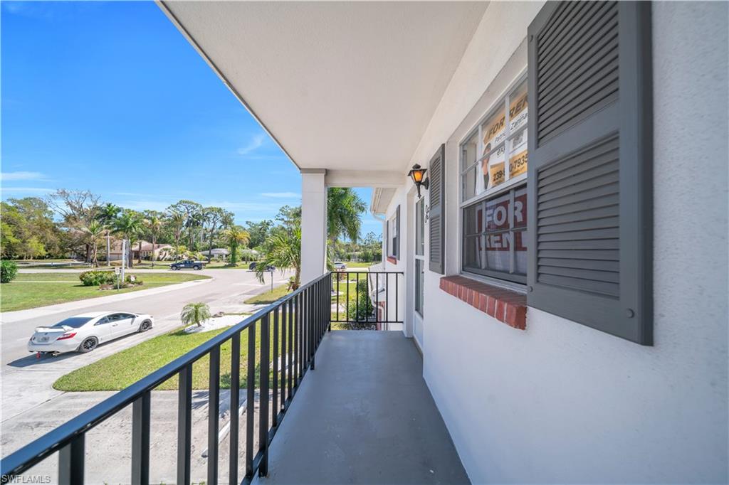 The property features a balcony with a black metal railing, offering views of the surrounding neighborhood with mature trees and a street
