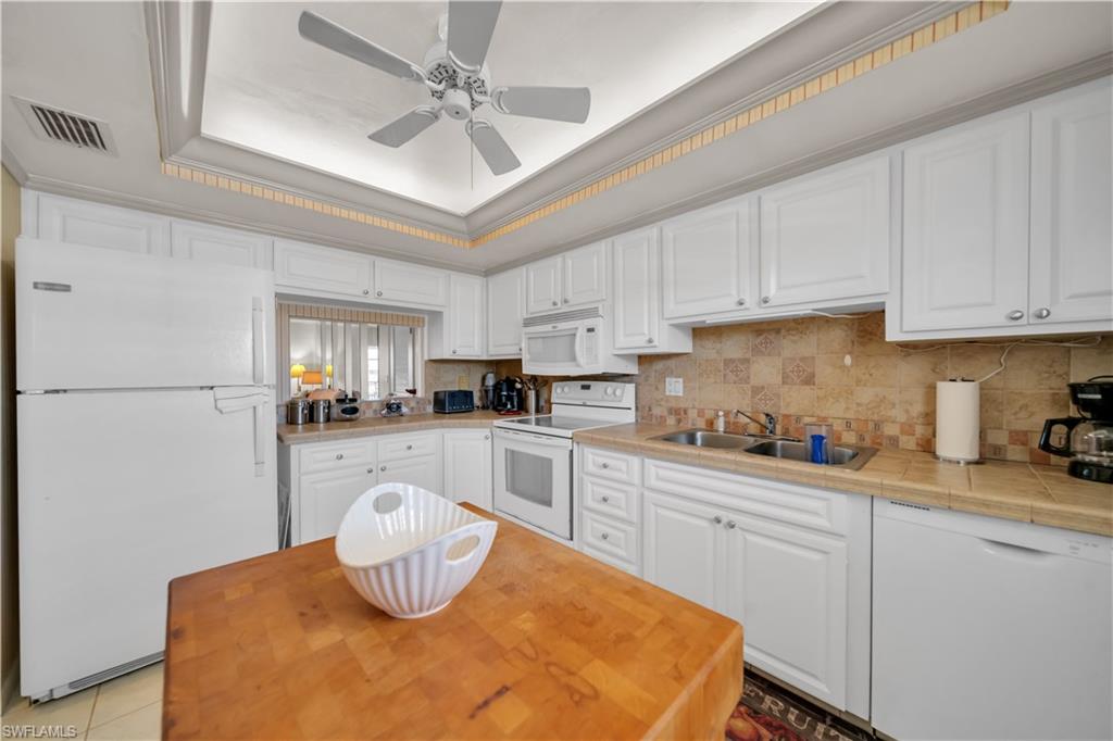 The kitchen features white cabinetry, a double basin sink, and a tiled backsplash