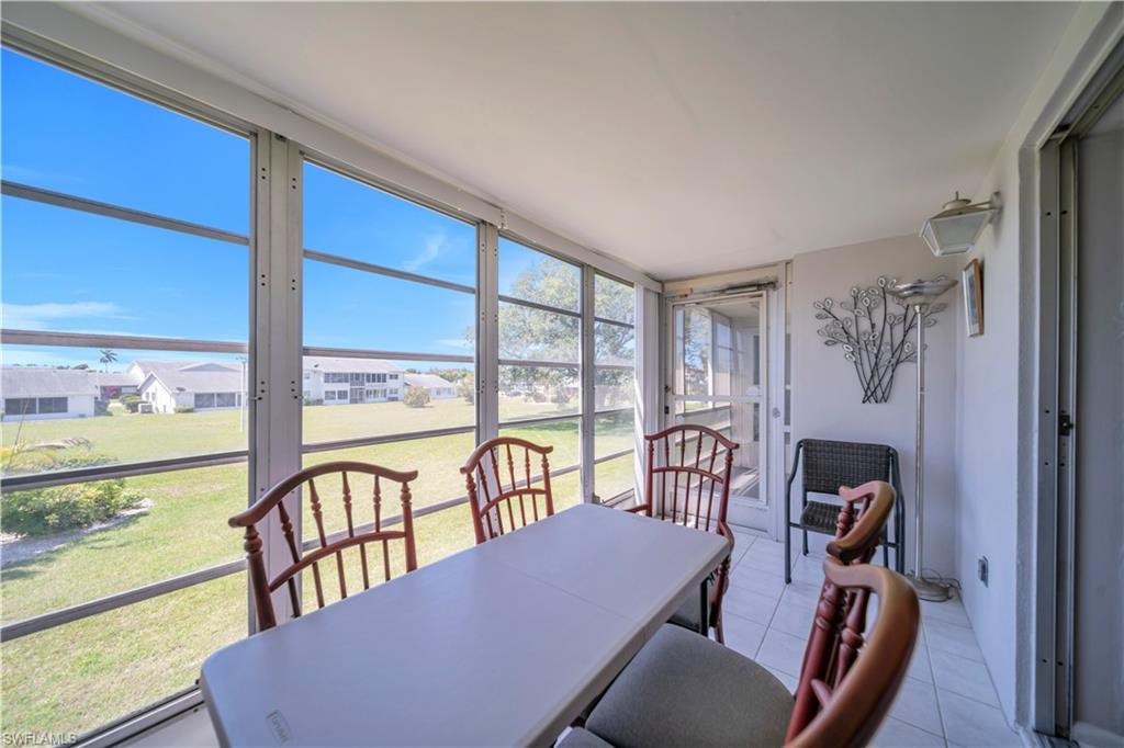 Enclosed sunroom with expansive windows providing views of the surrounding landscape, featuring tiled flooring and a door providing exterior access