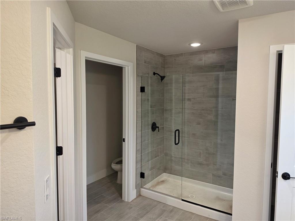Spacious bathroom featuring a glass-enclosed shower with tile surround and black fixtures, integrated ceiling lighting, and a separate water closet