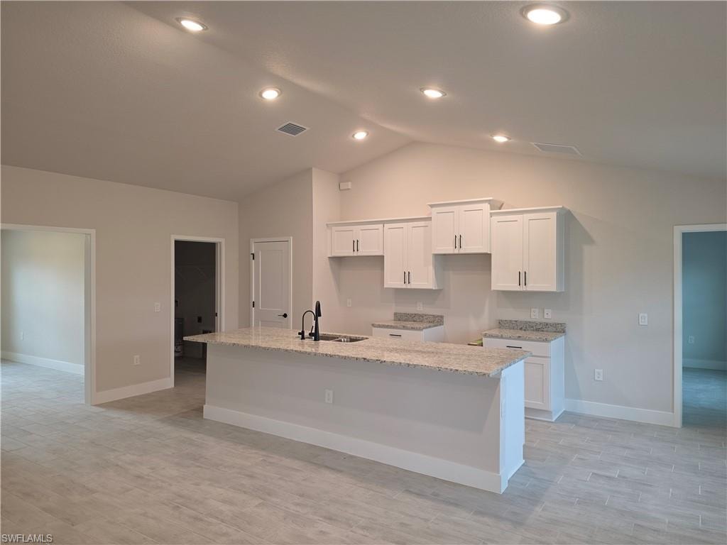 Kitchen featuring a granite-topped island with an undermount sink and matte black faucet, white shaker cabinetry, recessed lighting, and wood-finish tile flooring