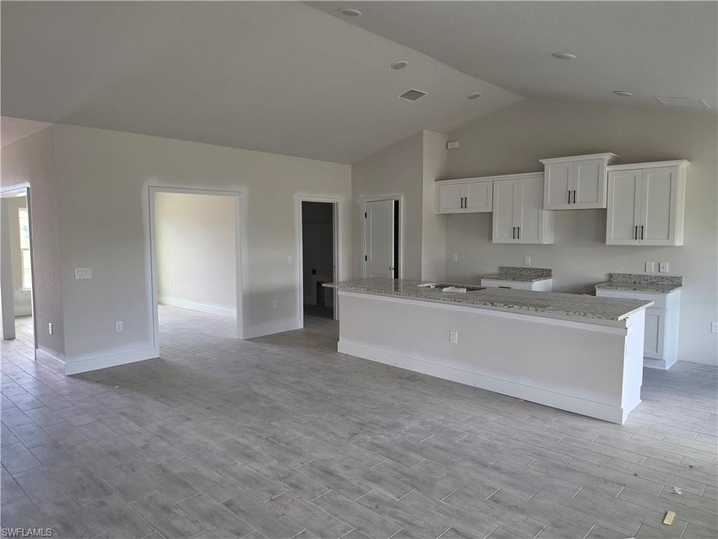 The open concept kitchen and living area features white cabinetry, granite countertops, and light-toned tile flooring