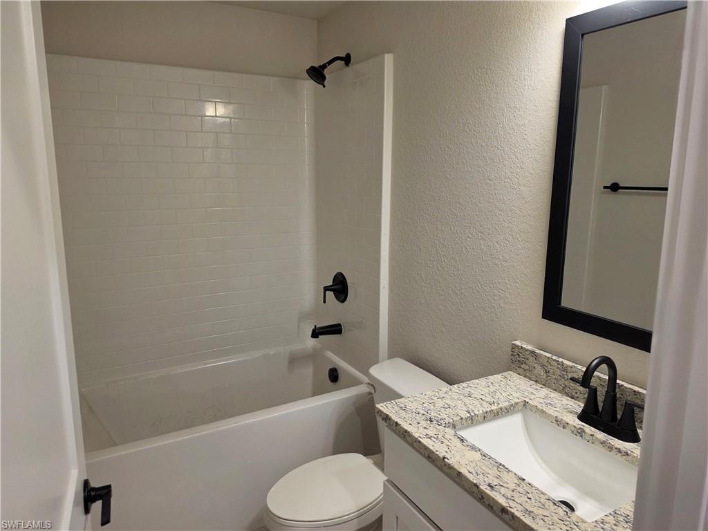 Bathroom featuring a white subway tile shower surround, matte black fixtures, integrated bathtub, vanity with undermount sink, and speckled countertop