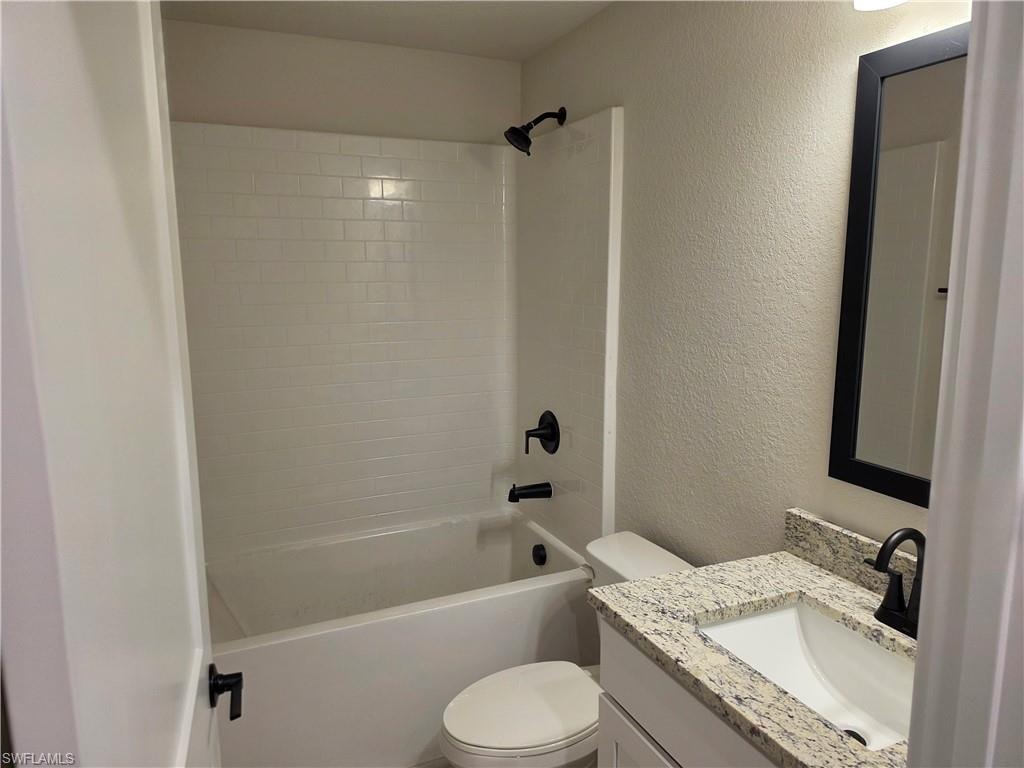 Bathroom featuring a white subway tile tub surround, black hardware, a granite countertop vanity, and a rectangular sink