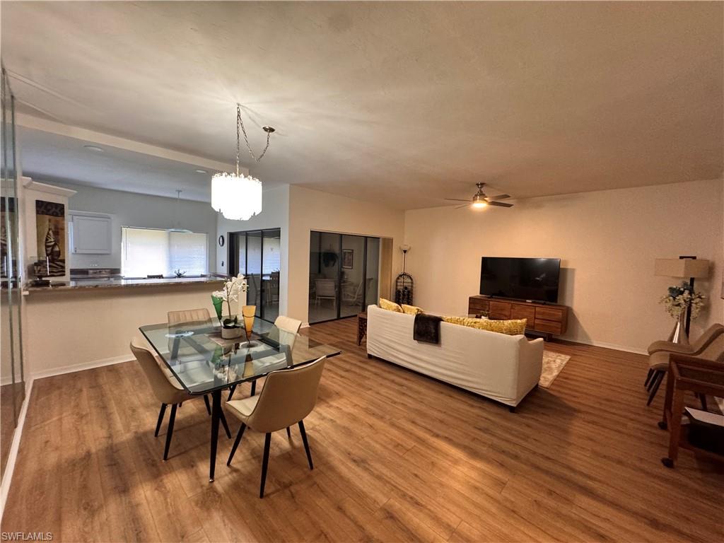 Open-concept living area featuring wood-finish flooring, a contemporary dining chandelier, and a breakfast bar with a stone-look countertop