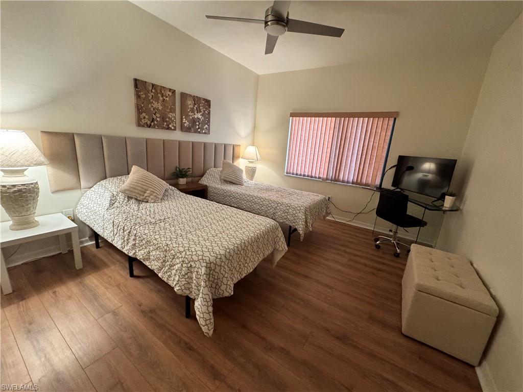 Vaulted ceiling bedroom featuring wood-finish flooring, a ceiling fan, and a window with vertical blinds