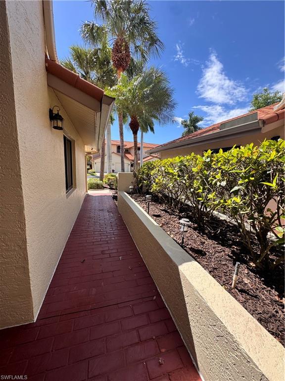 Brick-patterned pathway leading to the entrance, flanked by a stucco wall and a raised planter with established landscaping