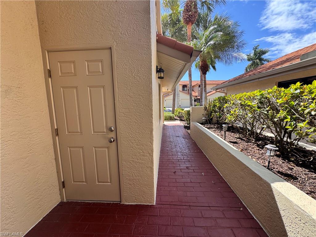 Exterior walkway featuring a red brick-patterned surface, textured stucco walls, and a built-in planter with established greenery