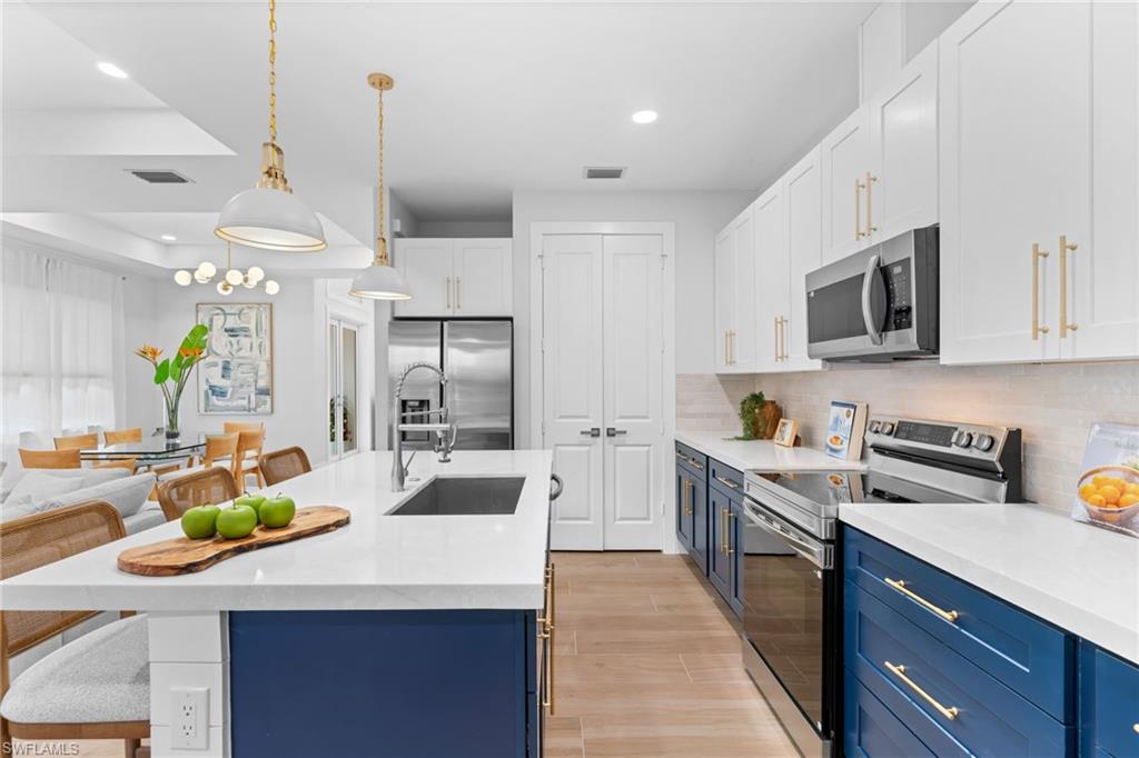Modern kitchen featuring a large central island with a sink, white countertops, stainless steel appliances, two-tone cabinetry, and wood-finish flooring